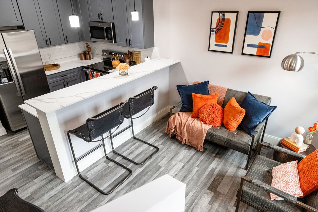 A modern kitchen with a white island and a grey and orange living room.