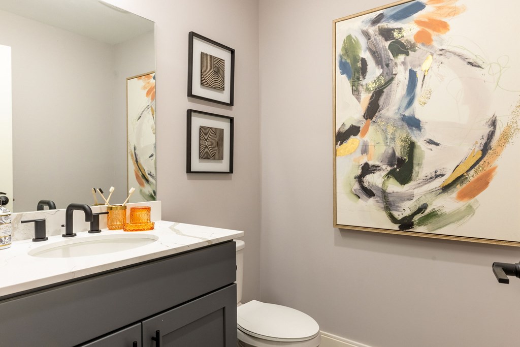 A bathroom with a toilet, sink, and two framed pictures on the wall.