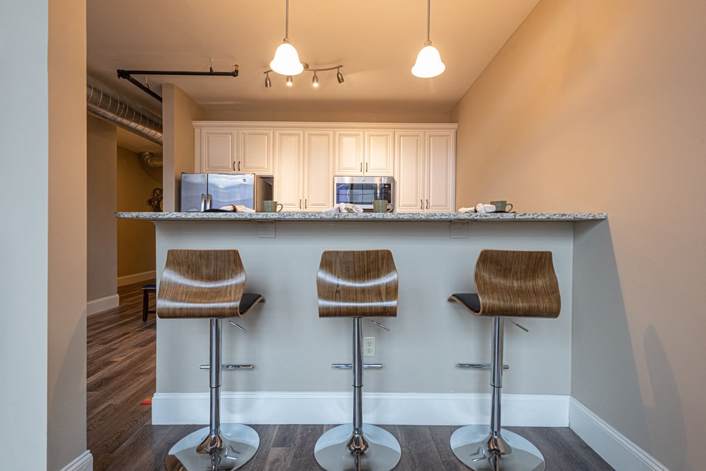a bar with three stools in front of a kitchen with a refrigerator and microwave
