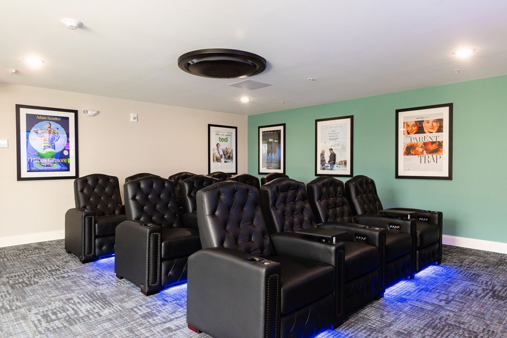 A row of black leather recliner chairs are lined up in a room with blue lights underneath them.