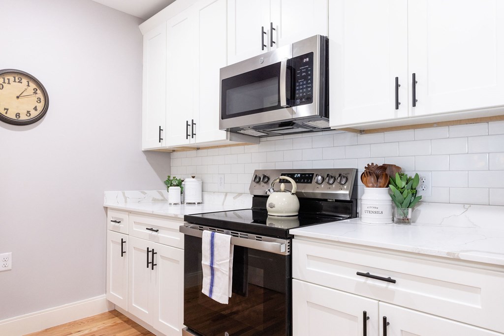 A white kitchen with a black stove top oven and a microwave above it.