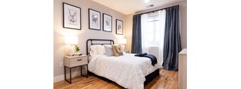 A bedroom with a large bed, a nightstand with a plant, and framed pictures on the wall.