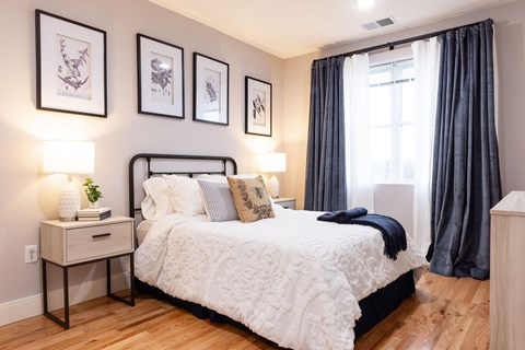 A bedroom with a large bed, a nightstand with a plant, and framed pictures on the wall.