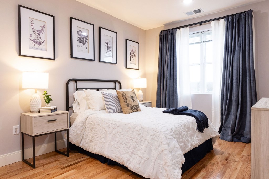 A bedroom with a large bed, a nightstand with a plant, and framed pictures on the wall.