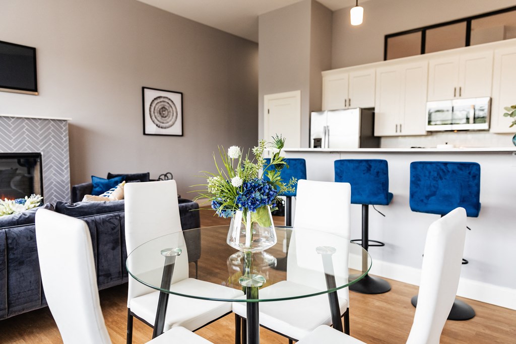 a dining table with white chairs and a glass table top with a vase of blue flowers