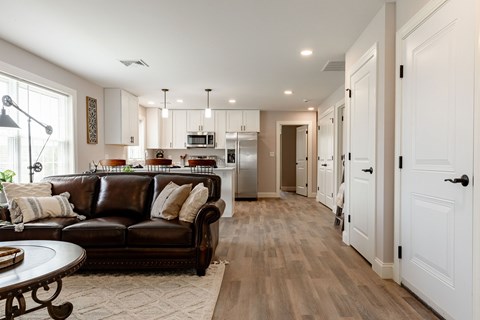 A modern living room with a brown leather couch and a kitchen in the background.