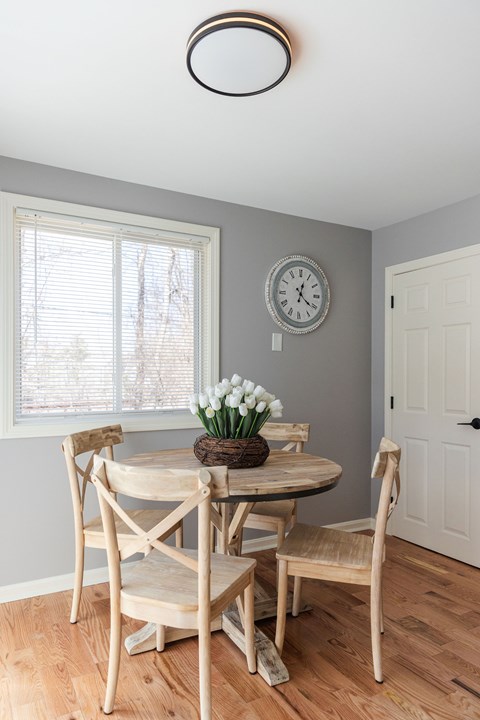 A dining room with a table set for two and a clock on the wall.