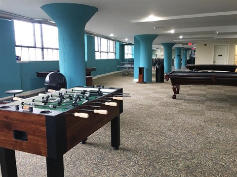 A foosball table is in the middle of a room with a pool table in the background.