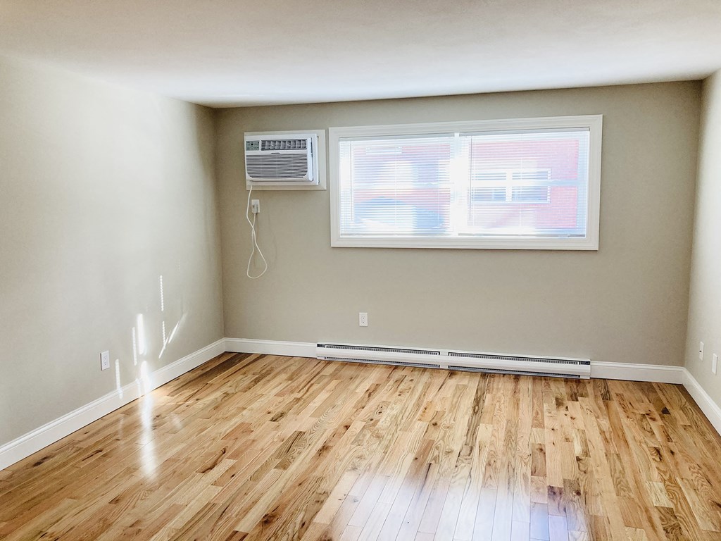 an empty room with wood floors and a window and a air conditioner
