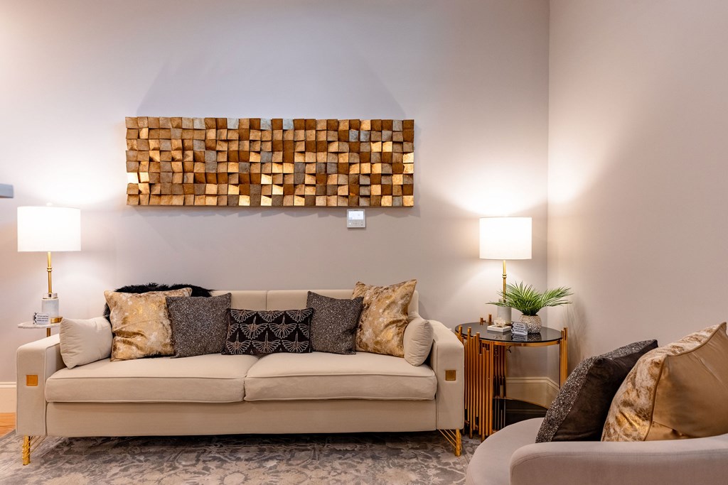 A living room with a beige couch, a wooden wall art, and two lamps.