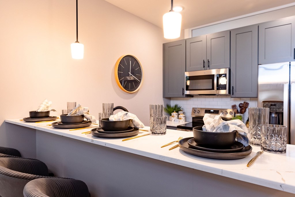 A modern kitchen with a clock on the wall and a dining table set for two.