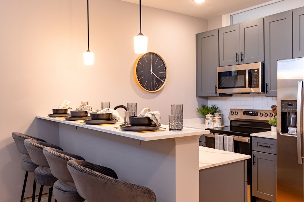 A modern kitchen with a bar area and grey chairs.