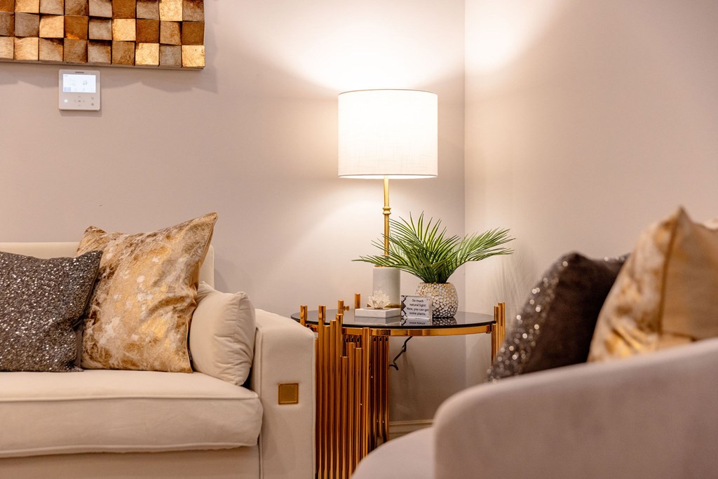A living room with a white couch, a small table with a plant, and a lamp.