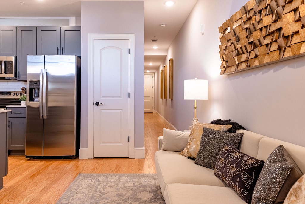 A modern kitchen with a refrigerator, a couch with pillows, and a wooden wall art.