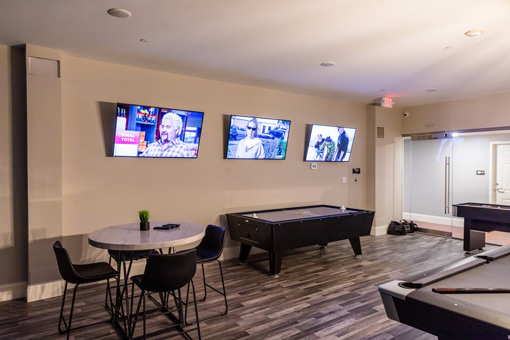 a game room with a pool table and televisions on the wall
