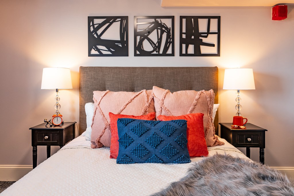 a bedroom with a bed with colorful pillows and artwork on the wall above it