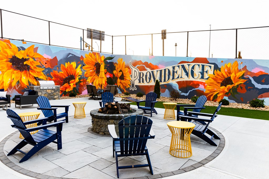 a patio with blue chairs and yellow tables and a fire pit