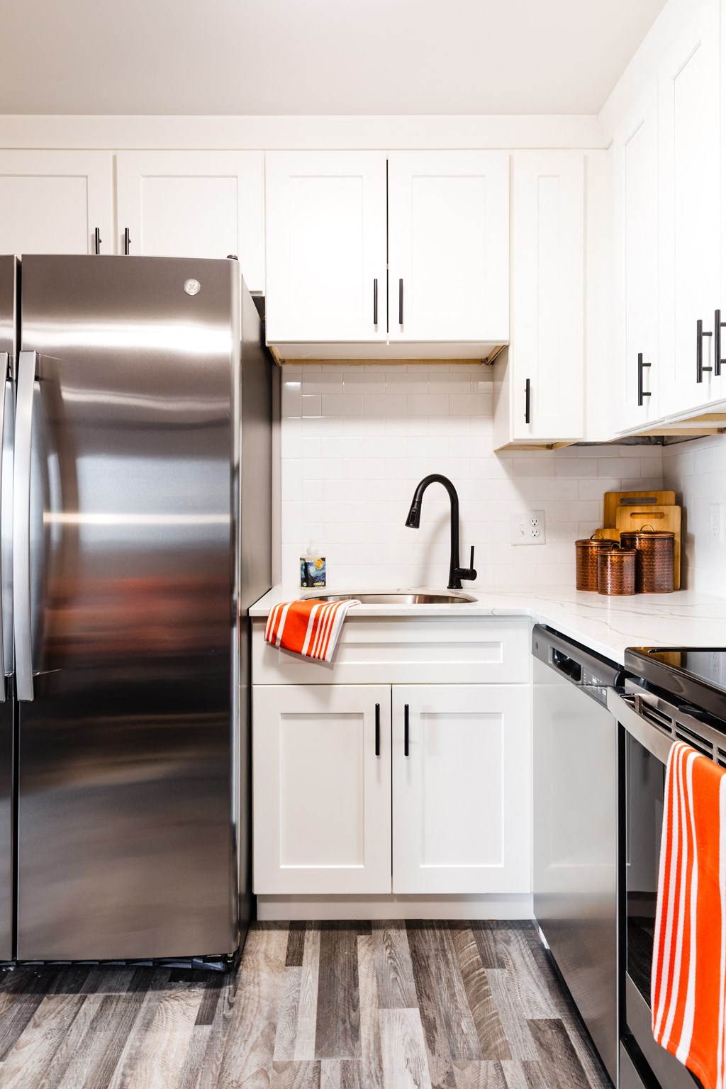 a kitchen with white cabinets and a stainless steel refrigerator    and orange towels