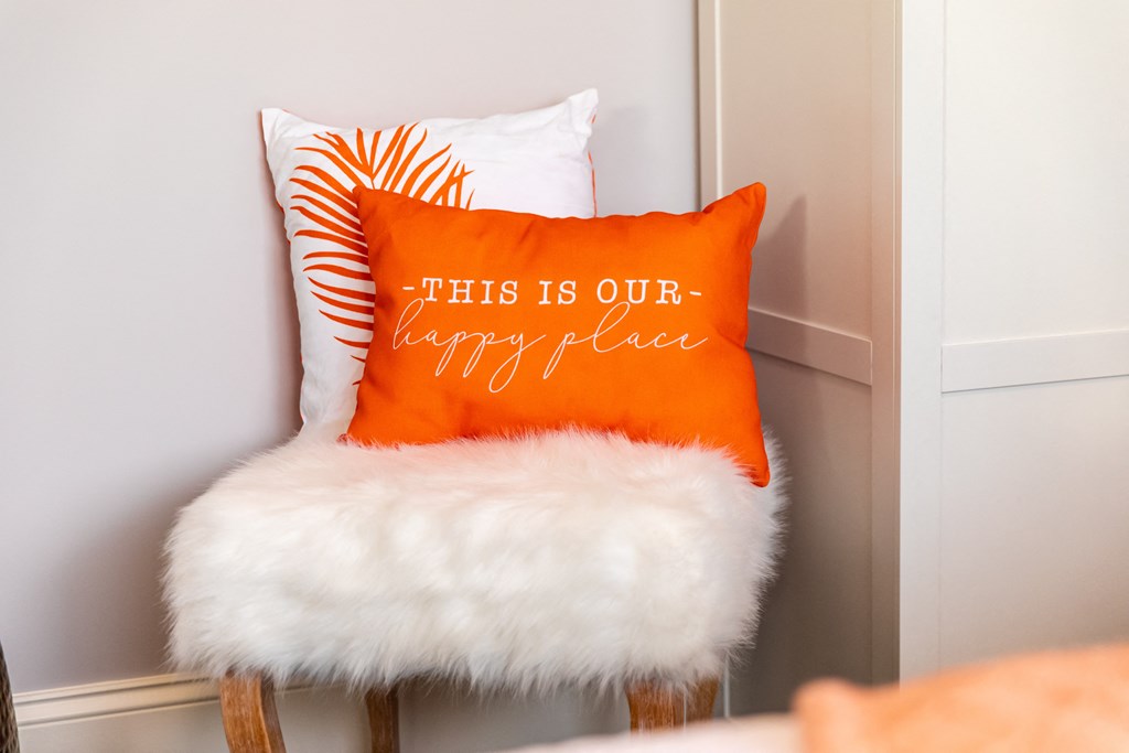 a orange and white pillow sitting on a chair with a white furry seat