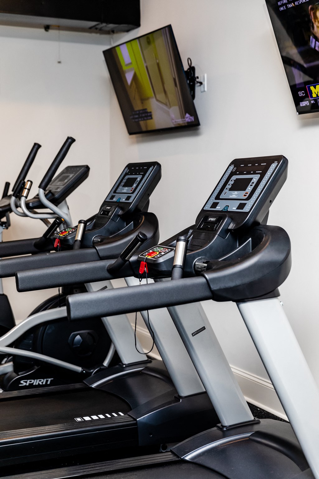 a row of treadmills in a gym with a tv on the wall