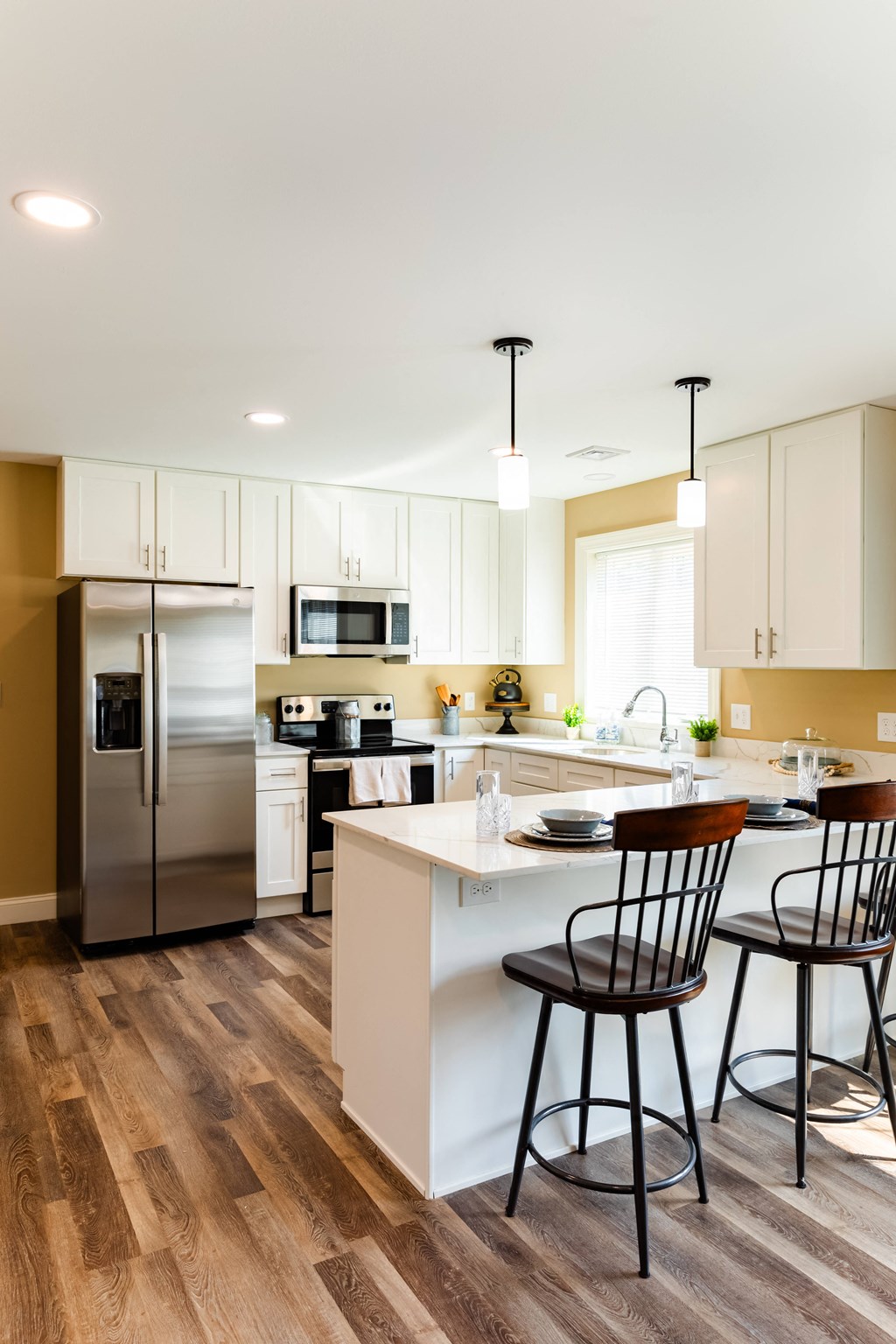a kitchen with white cabinets and a island with three chairs