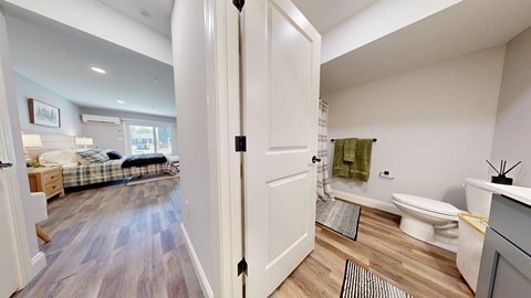 A bathroom with a toilet, sink, and a bedroom with a bed and dresser.
