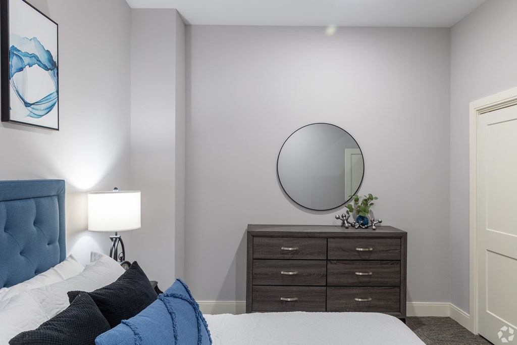 A bedroom with a bed, a dresser, and a round mirror on the wall.