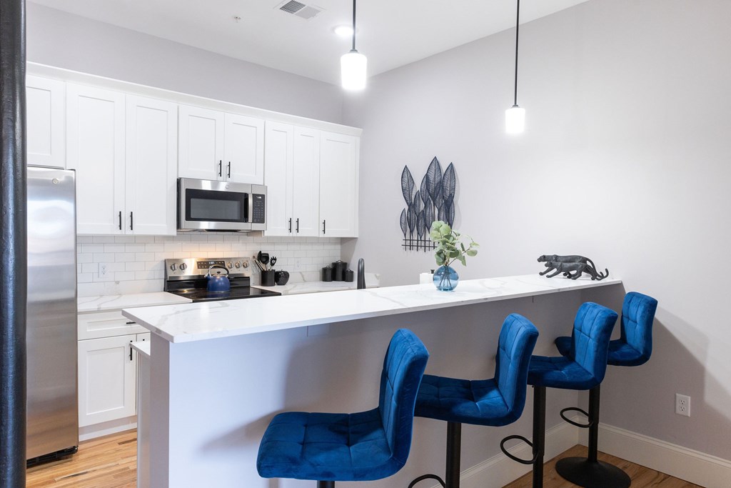 A kitchen with white cabinets and a white island with blue chairs.
