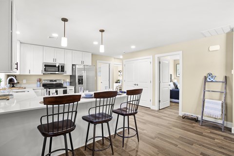 a kitchen with white cabinets and a bar with three stools