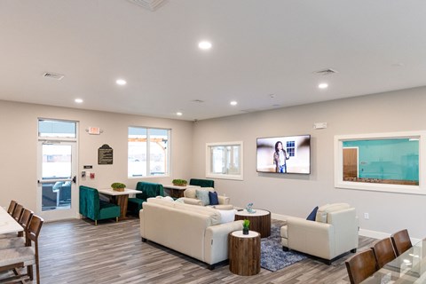 A spacious living room with a white sofa set and a television mounted on the wall.