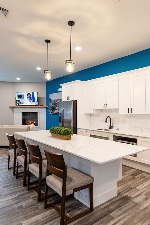 A modern kitchen with a long white island and wooden chairs.