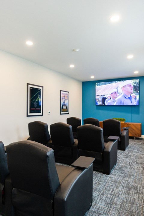A room with black leather chairs and a screen on the blue wall.
