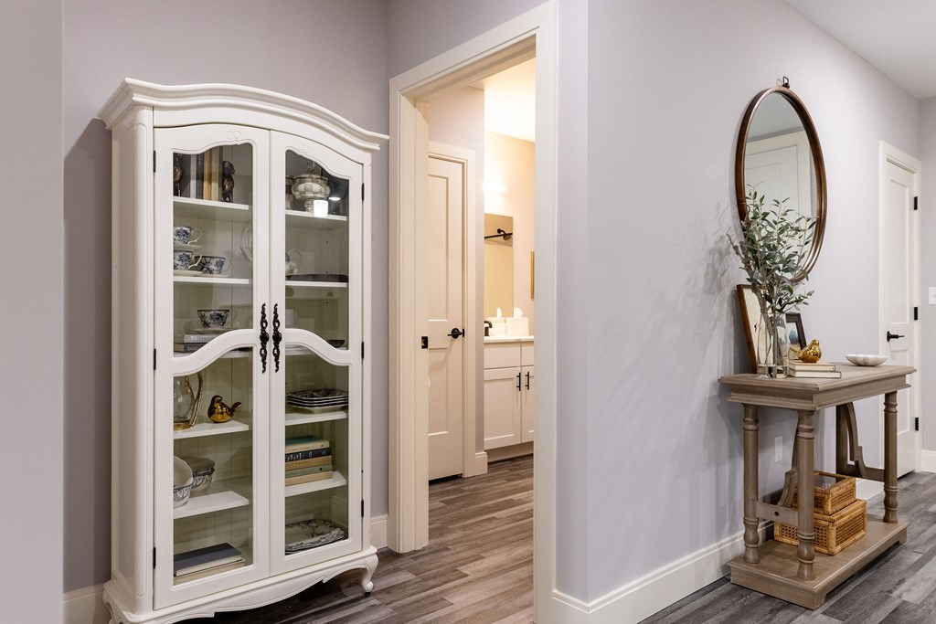 A white china cabinet with glass doors stands in a room with a table and mirror.