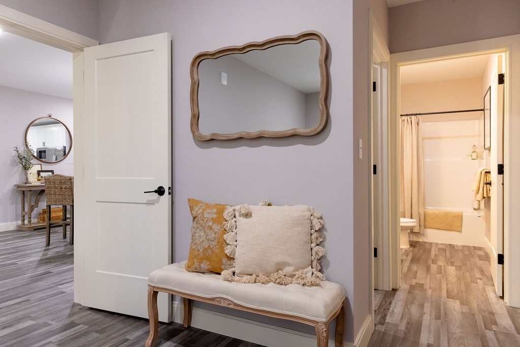 A white door with a mirror above it and a bench with a pillow on it.