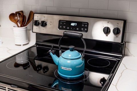 A blue tea kettle is on a black stove.