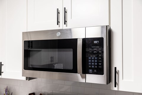 A stainless steel microwave with digital display and control panel is mounted on a kitchen wall.
