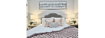 A bed with a grey headboard and a white comforter with a grey blanket on top.