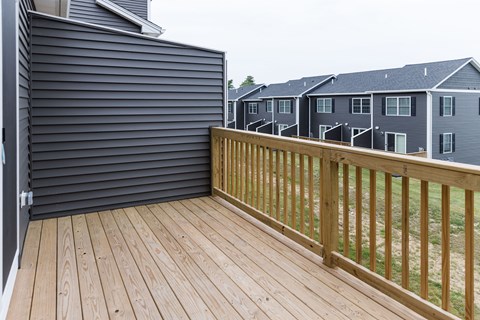 A wooden deck with a railing and a grey house in the background.