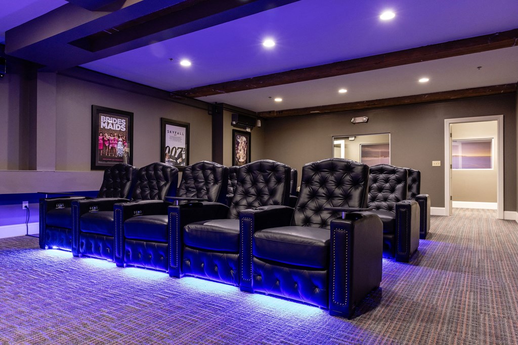 A row of black leather chairs are lined up in a room with purple lighting.