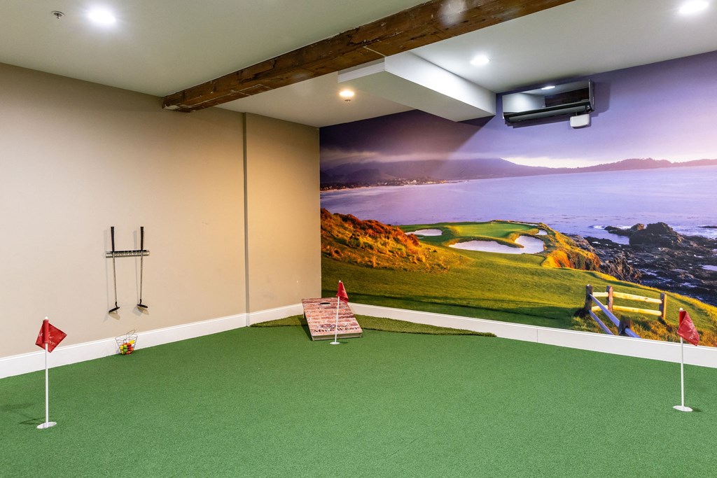 A room with a golf simulator and a green carpet.