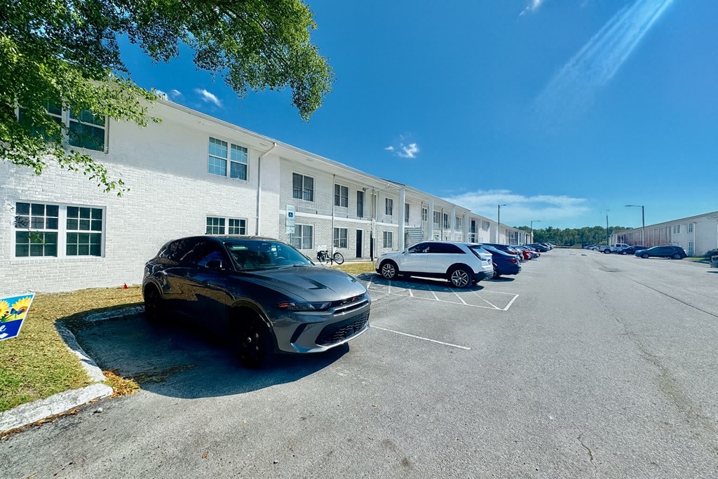 A black car is parked in a parking lot in front of a white building.