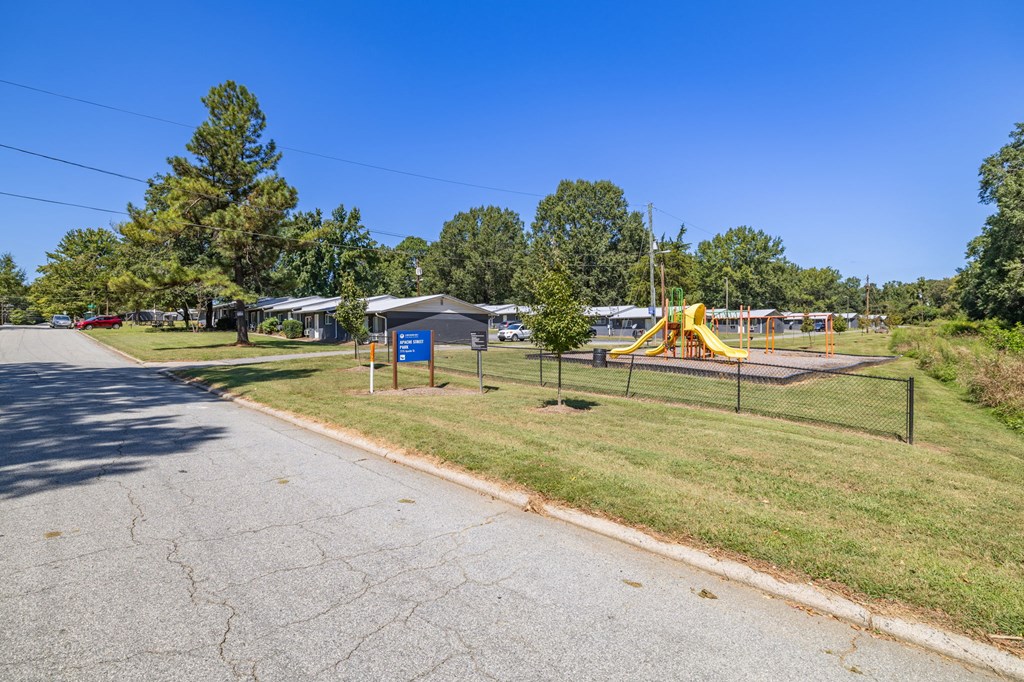 A playground with a yellow slide is located next to a road.