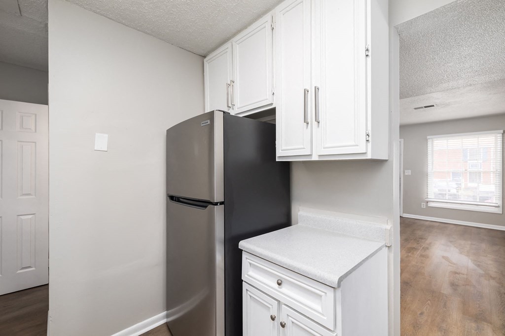 an empty kitchen with a refrigerator and white cabinets