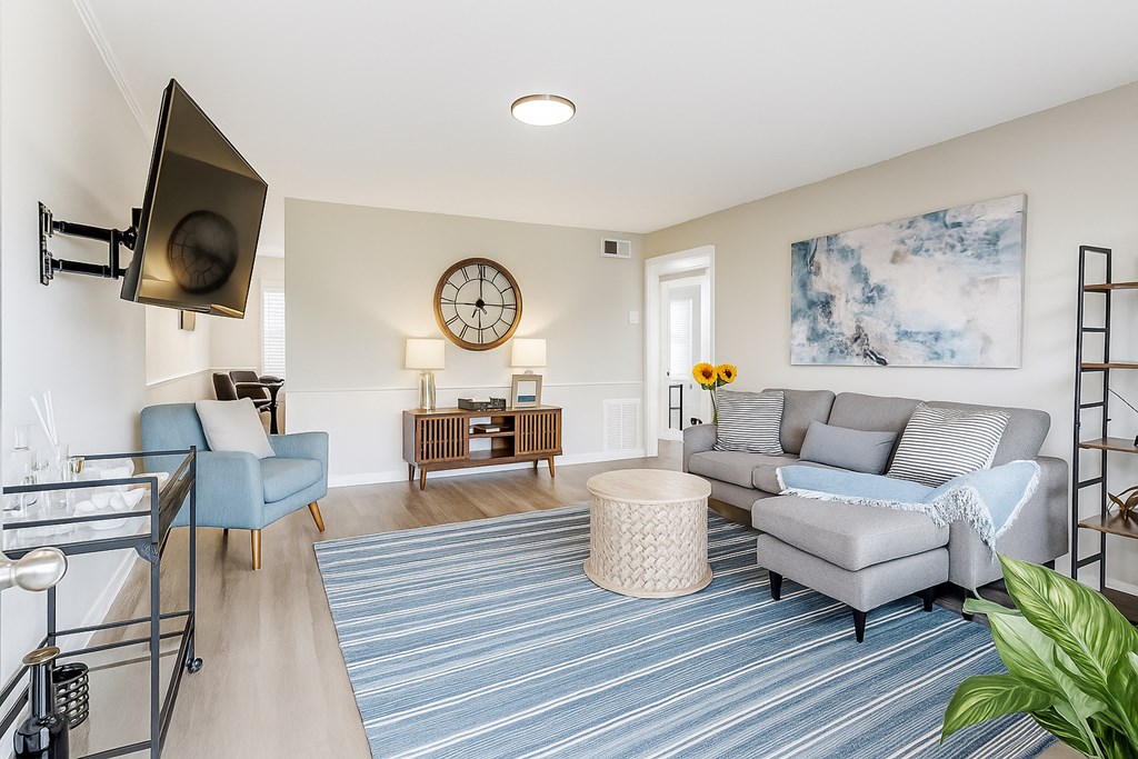 A living room with a grey couch, a blue chair, and a clock on the wall.