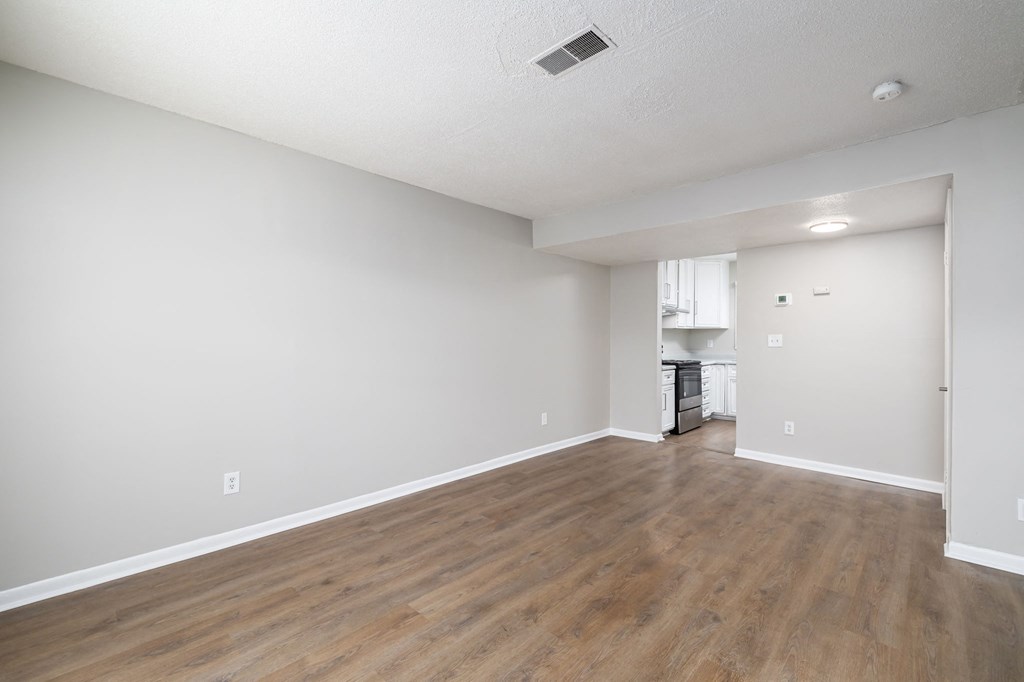 an empty living room and kitchen with wood floors and white walls