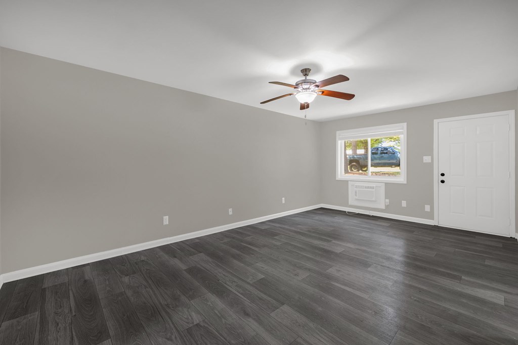 A room with a ceiling fan and a window showing a parking lot.