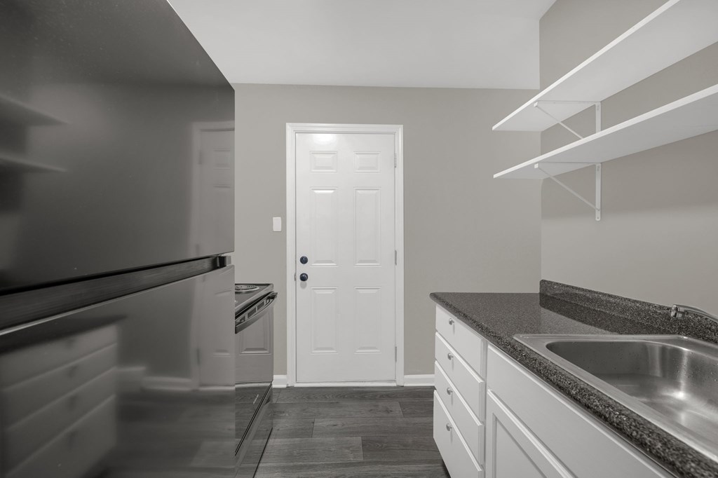 A kitchen with a black refrigerator, white door, and a granite countertop.