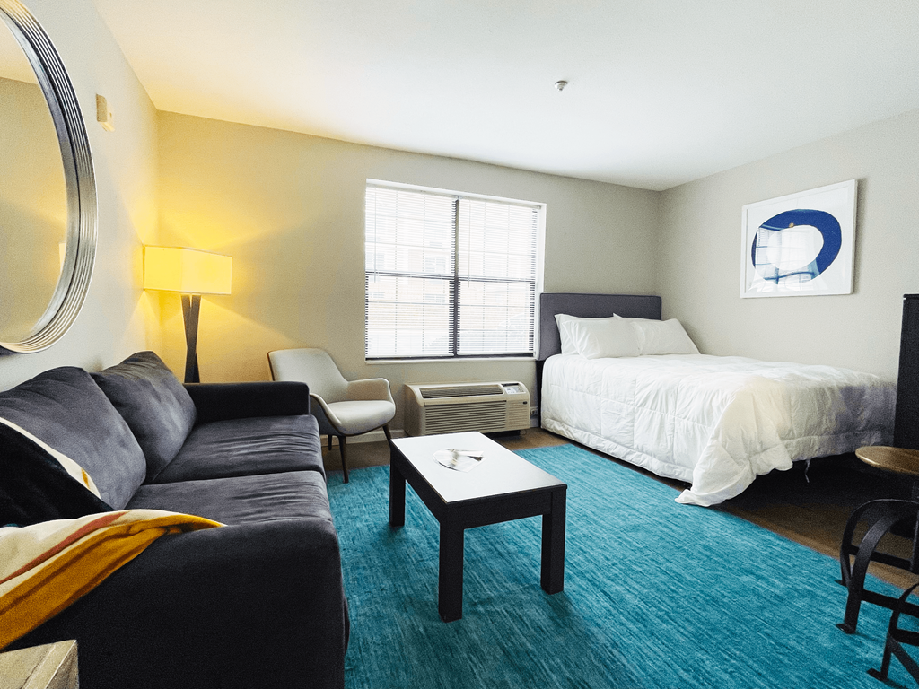 A well lit bedroom with a bed, chair, couch and a table.