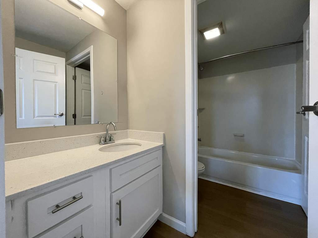 A white bathroom with a sink, mirror, and bathtub.