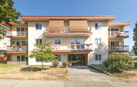 A large white apartment building with balconies and a driveway in front.